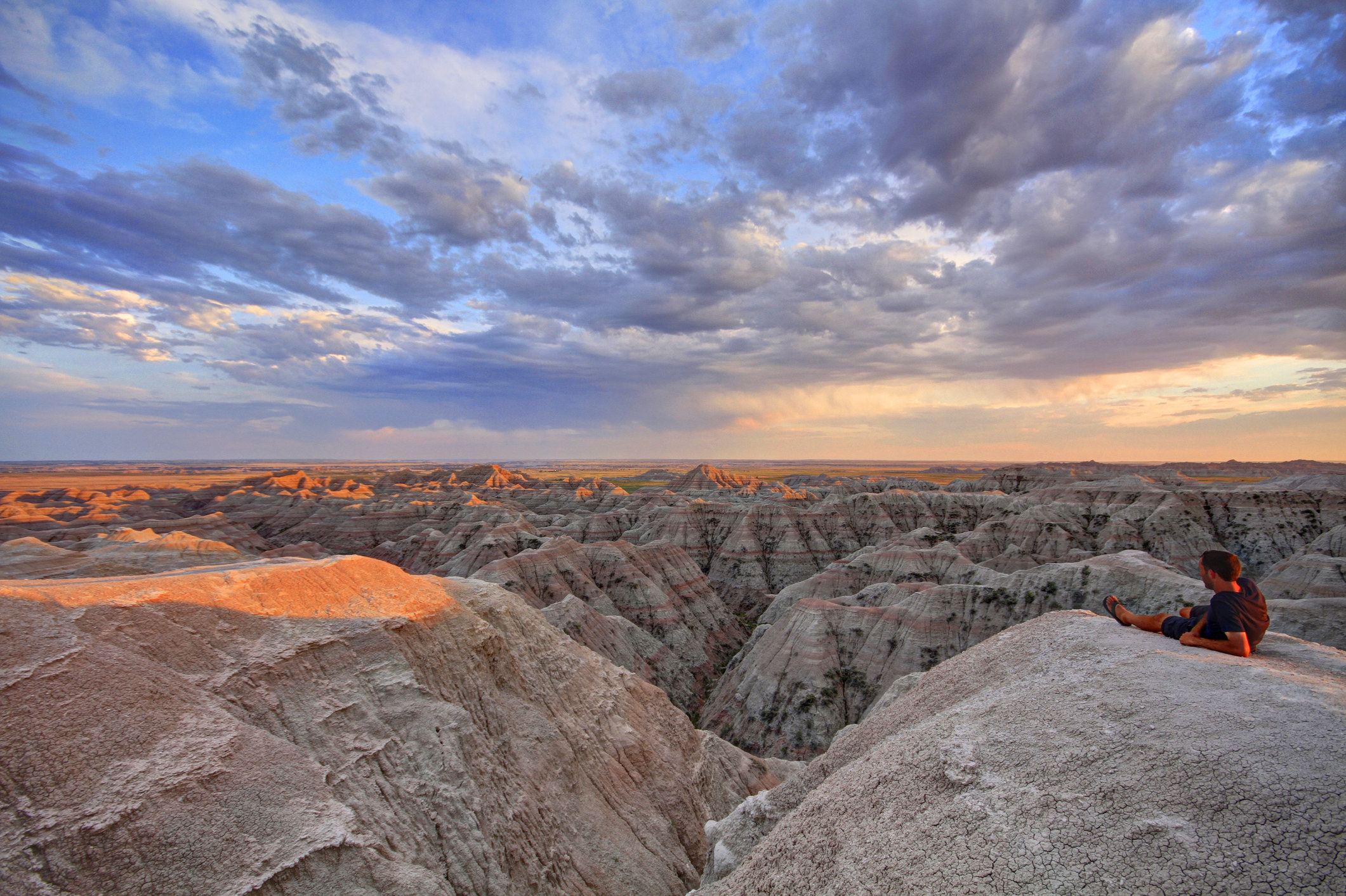 A man reclines on a rock overlooking rocky badlands during sunset