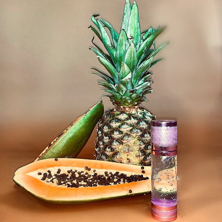 the bottle in front of a papaya half and a whole pineapple