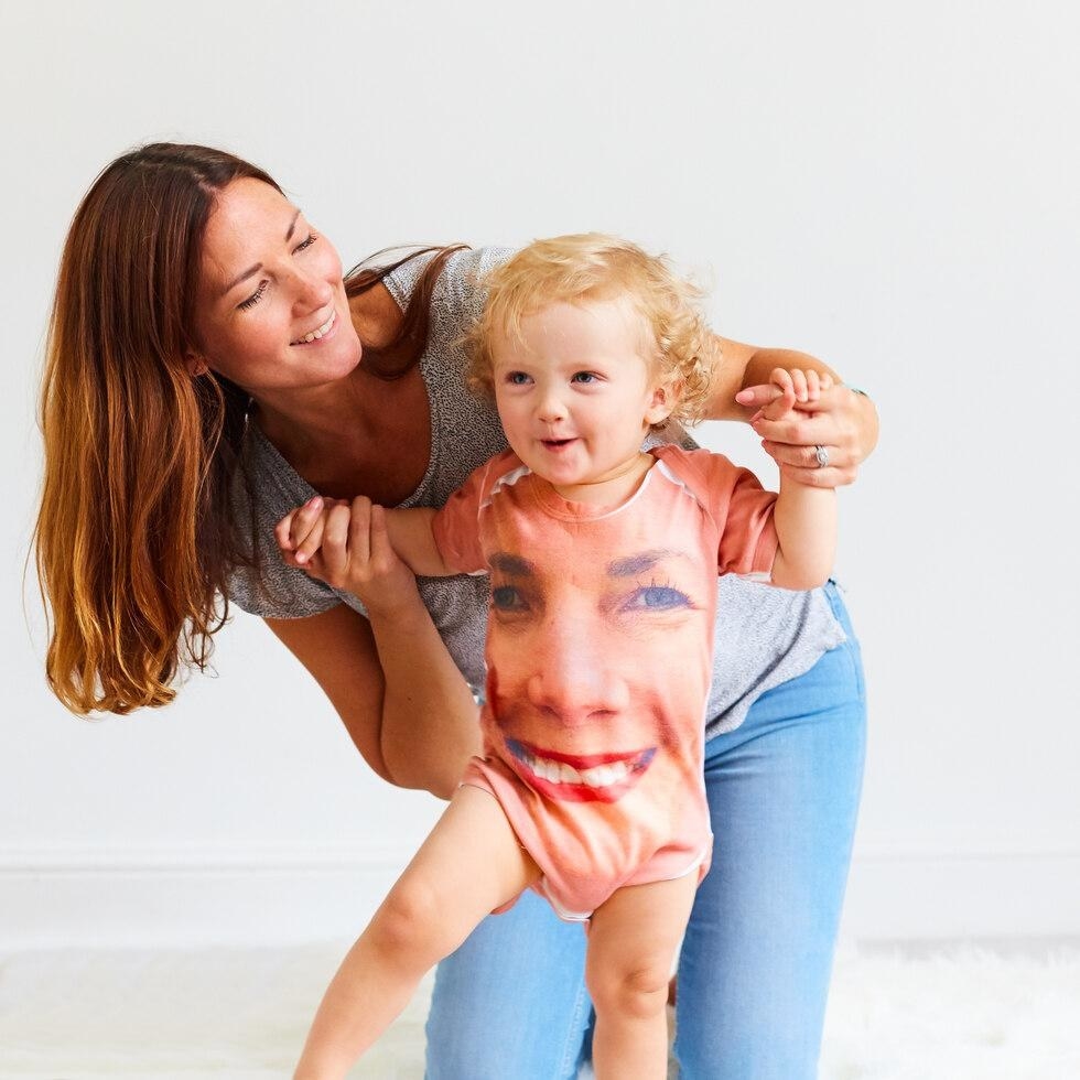 A baby wears a onesie featuring a giant image of their mother&#x27;s face