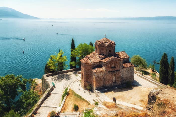 An old brick monastery set on a cliff overlooking a giant blue lake dotted with boats