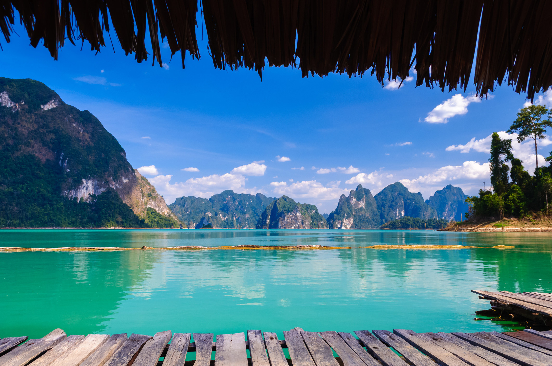 A photo taken from the wooden deck of a floating hut, looking out on a turquoise lake dotted with jagged mountains