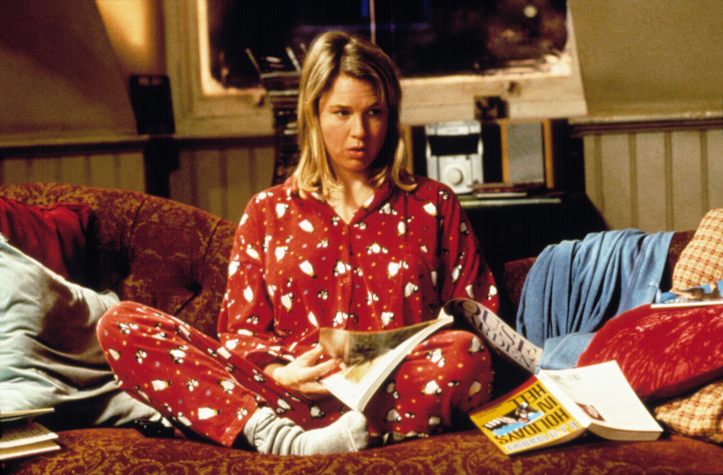 Still from Bridget Jones&#x27;s Diary: Renee Zellweger sits on a couch in pyjamas and socks reading a magazine