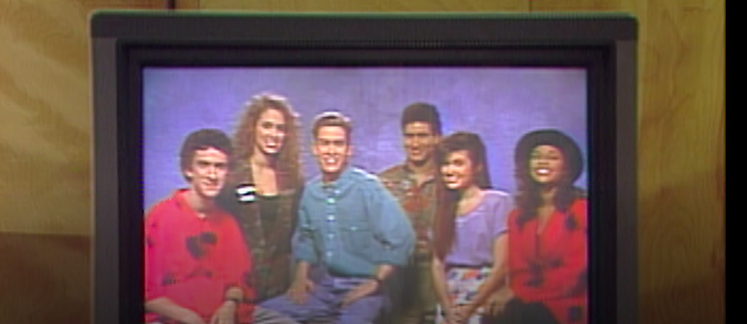 The original cast appears on a video screen