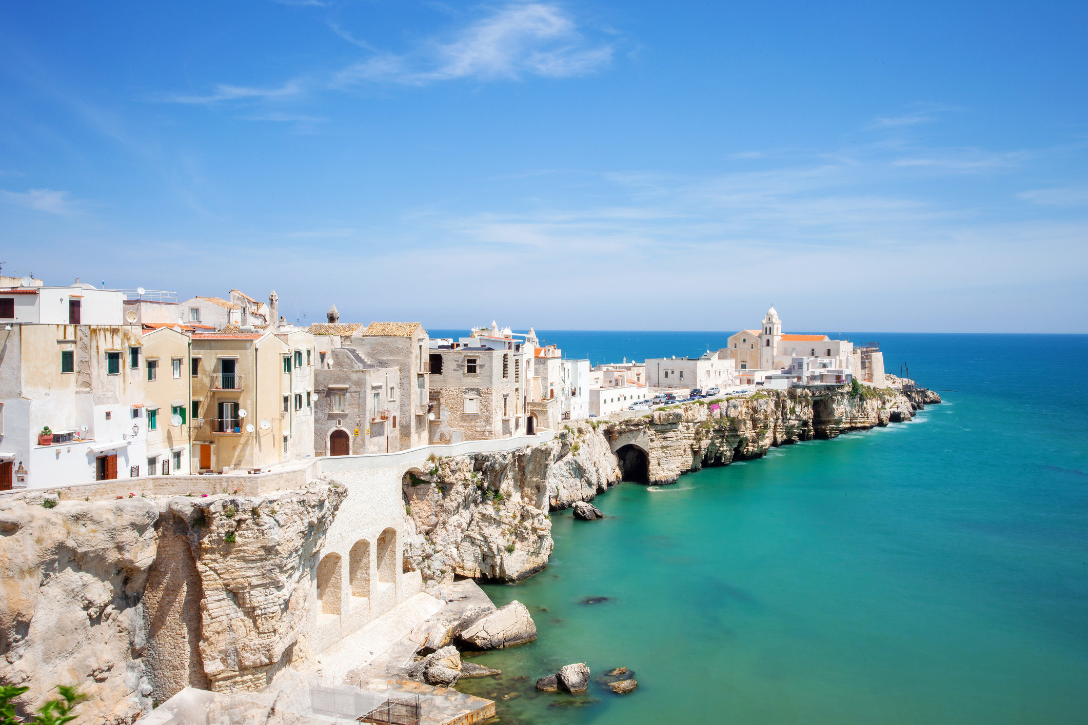 A rocky peninsula jutting into blue sea, with white square buildings