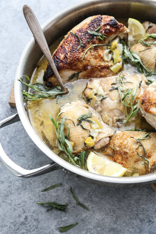 A skillet of braised chicken thighs in a creamy ginger leek sauce sprinkled with fresh herbs.