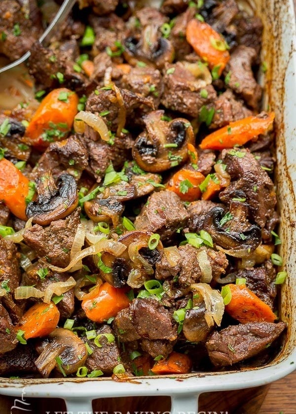 A casserole dish filled with roasted beef, carrots, mushrooms, scallions, and caramelized onions.