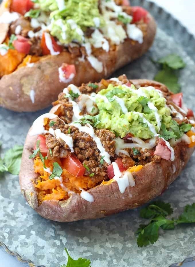 Two sweet potatoes stuffed with ground beef, tomatoes, guacamole, and topped with sour cream and cilantro.