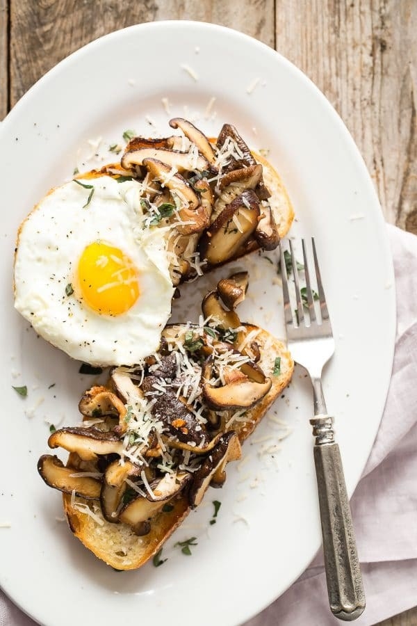 Two slices of toast topped with mushrooms, cheese, and a fried egg.