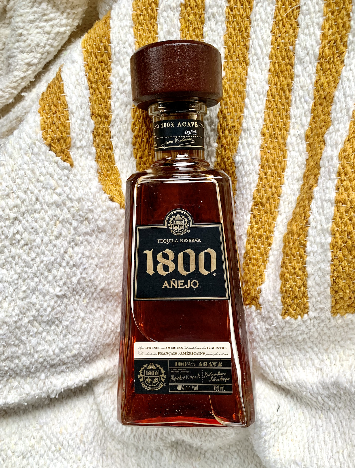 A bottle of 1800 Anejo against a a white and yellow fabric.