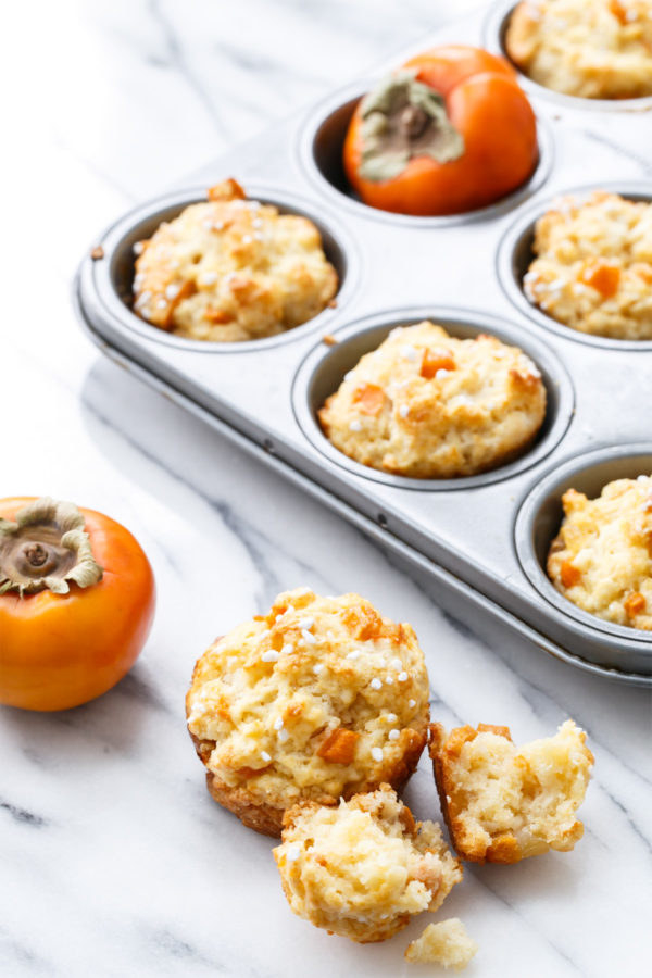 A muffin tray filled with ginger persimmon scone muffins and one crumbled muffin on the side.
