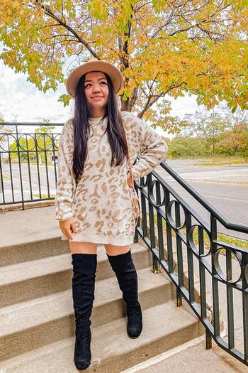 A reviewer wearing the sweater in cream and tan as a minidress with tall boots