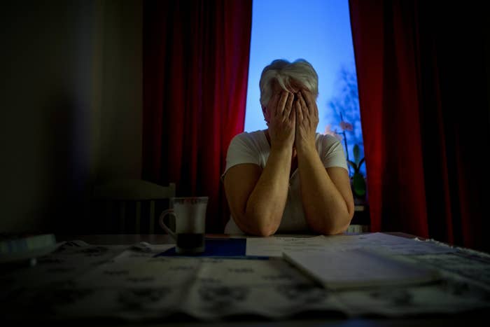 A woman sits in front of a window with her head in her hands