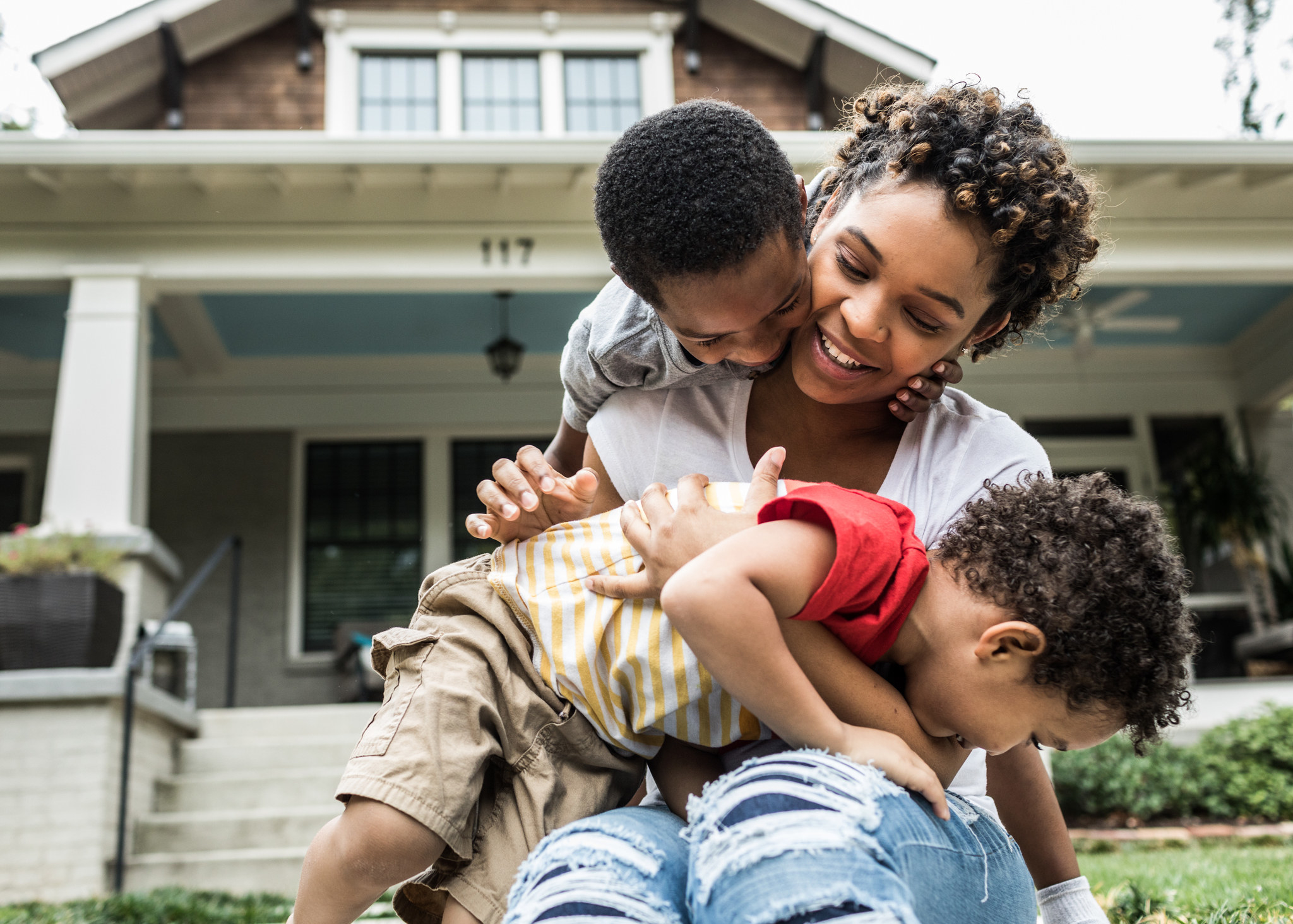 Single mother playing with young sons in front of house.