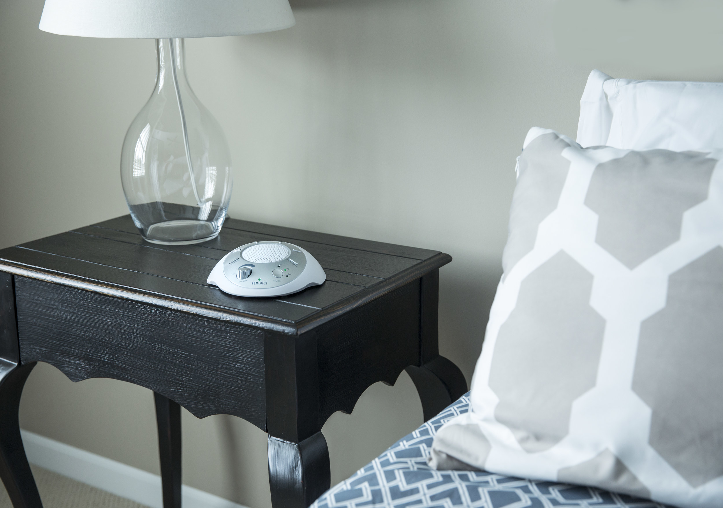 the white noise machine on a night table next to a bed