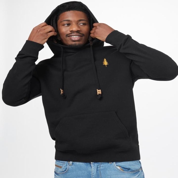 a model wearing the black fleece hoodie with a golden spruce tree design 