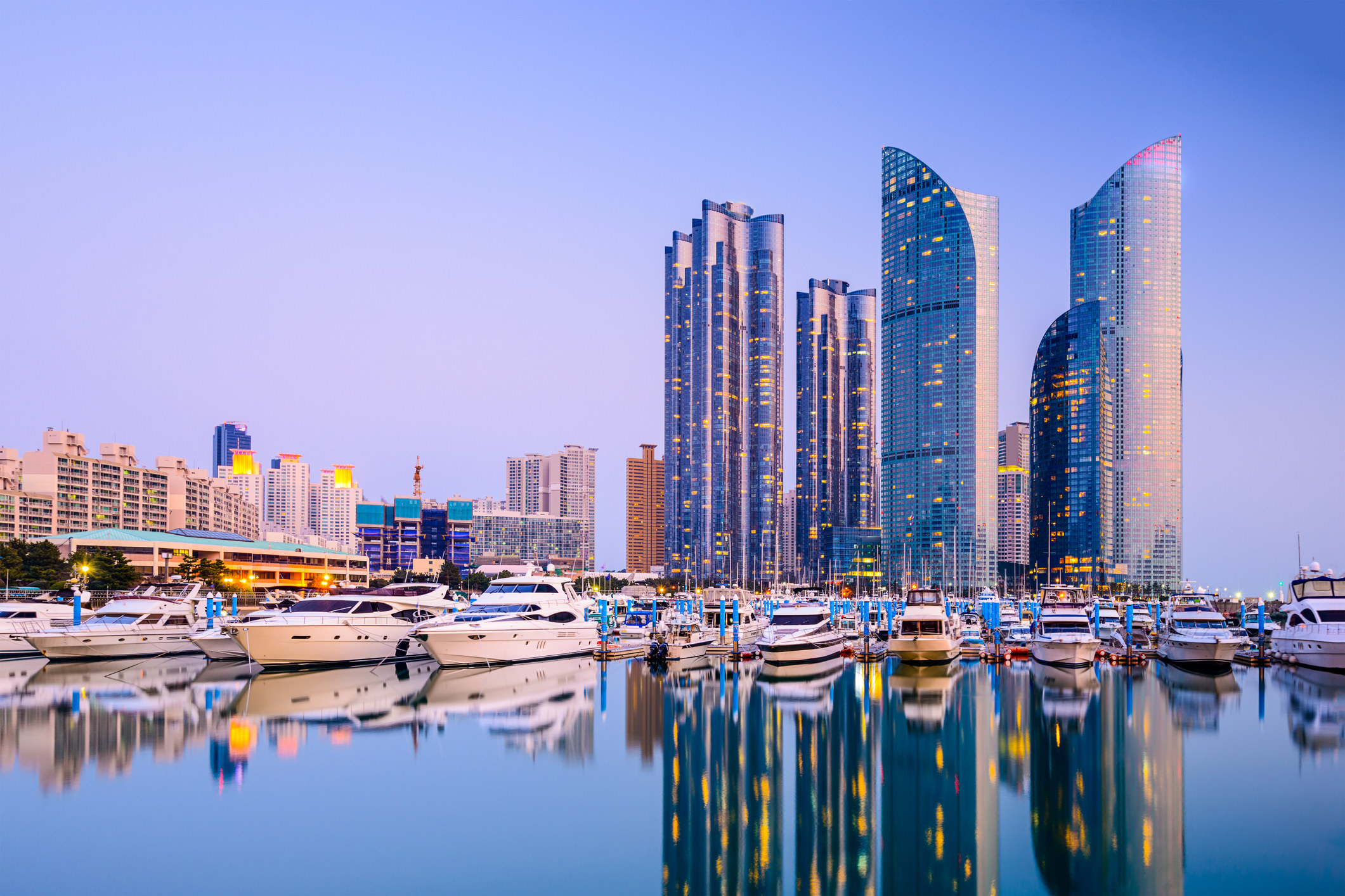 Tall skyscrapers line a harbor filled with boats at twilight