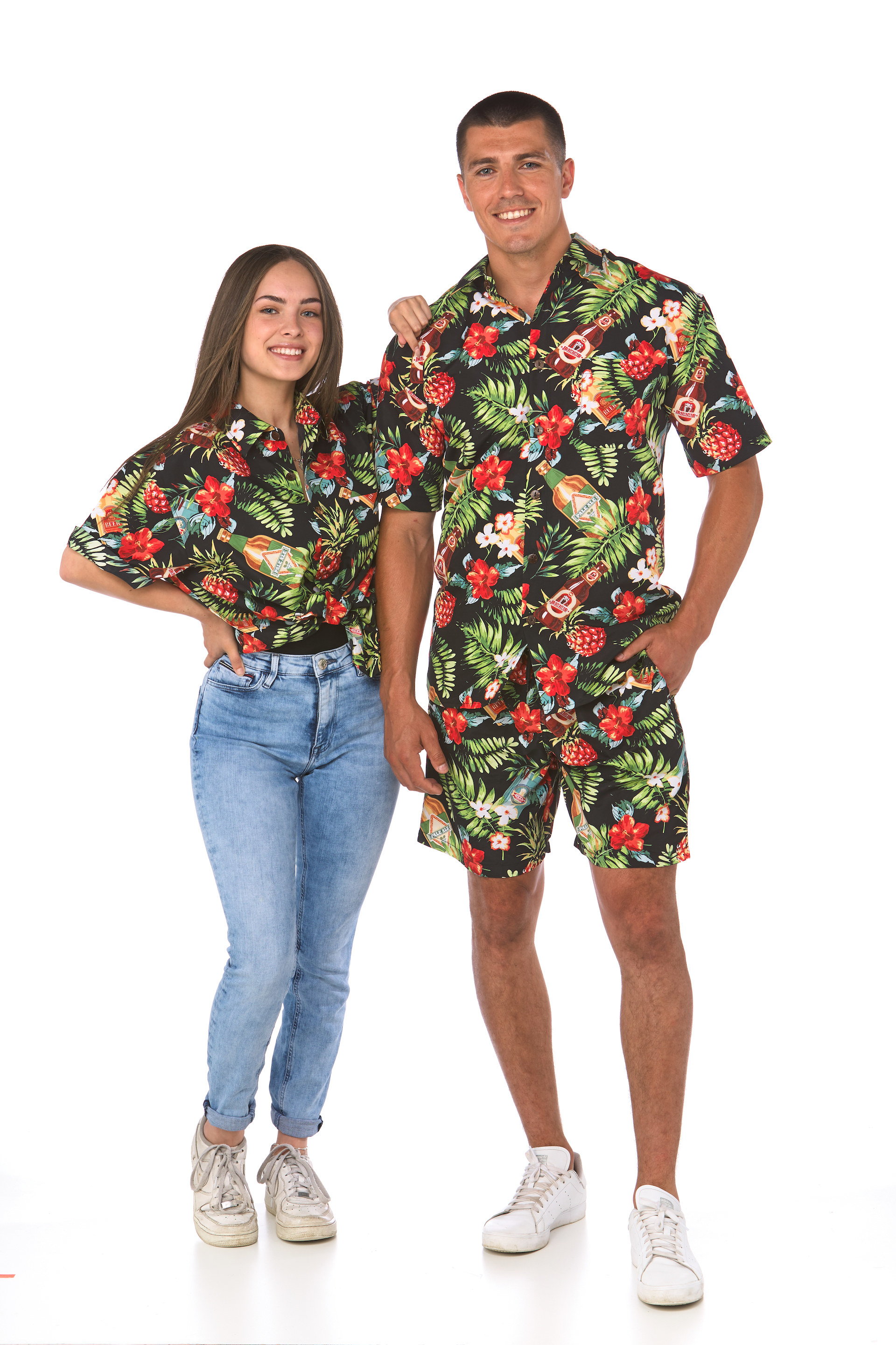 Man and woman in matching shirts with a dark background, palm fronds, flowers and beer