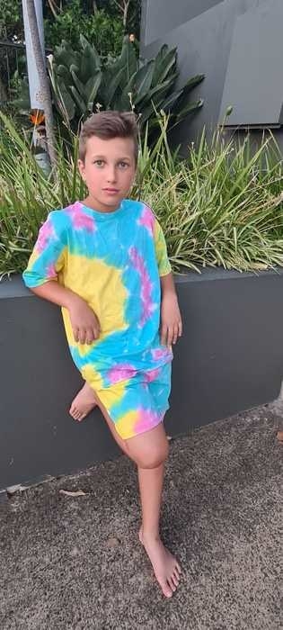 Kid leaning against a wall showing off a matching shirt and shorts pastel tie dye number