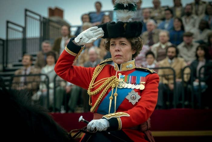Olivia Colman as Queen Elizabeth; she is riding a horse and is doing a salute