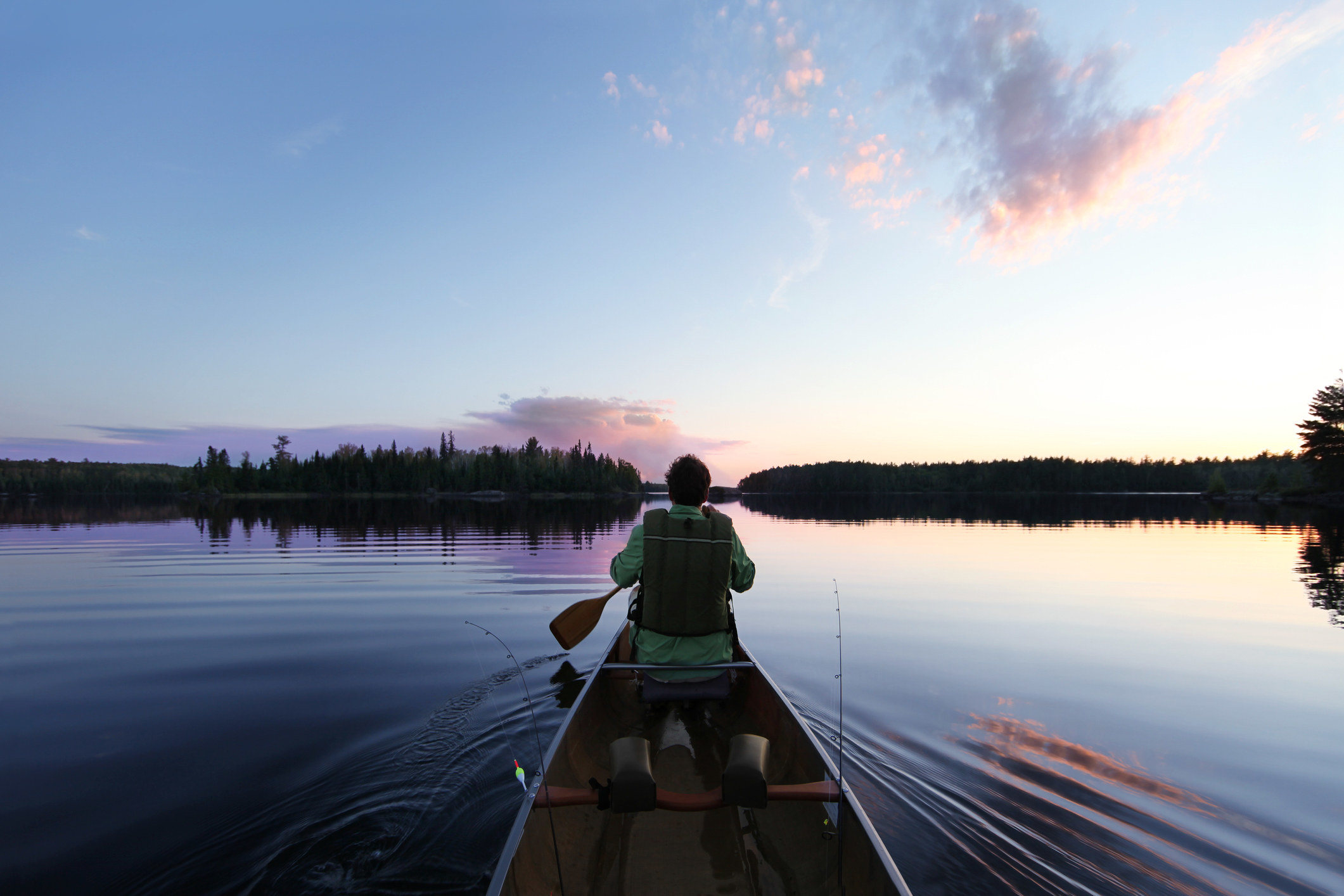 Person canoeing at dusk in flat waters