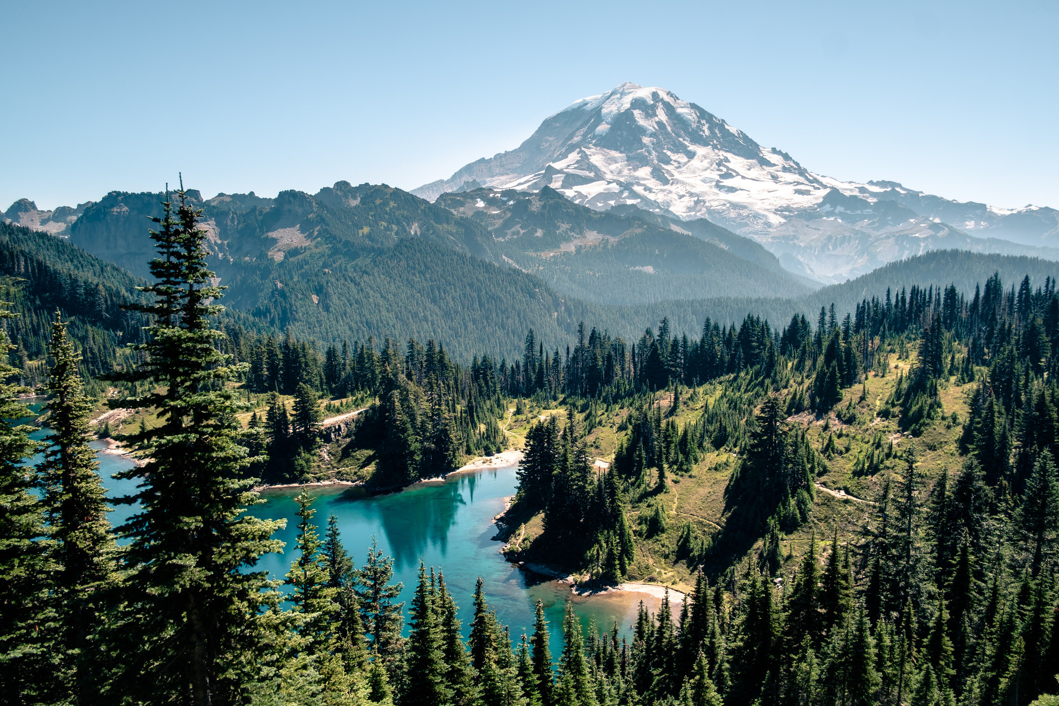 Water and tree-covered hills leading to snow-covered mountain