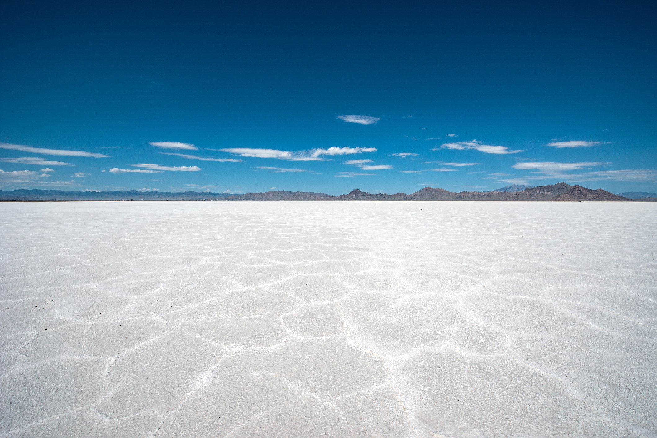 Flat, white earth leading to mountains with a blue sky overhead