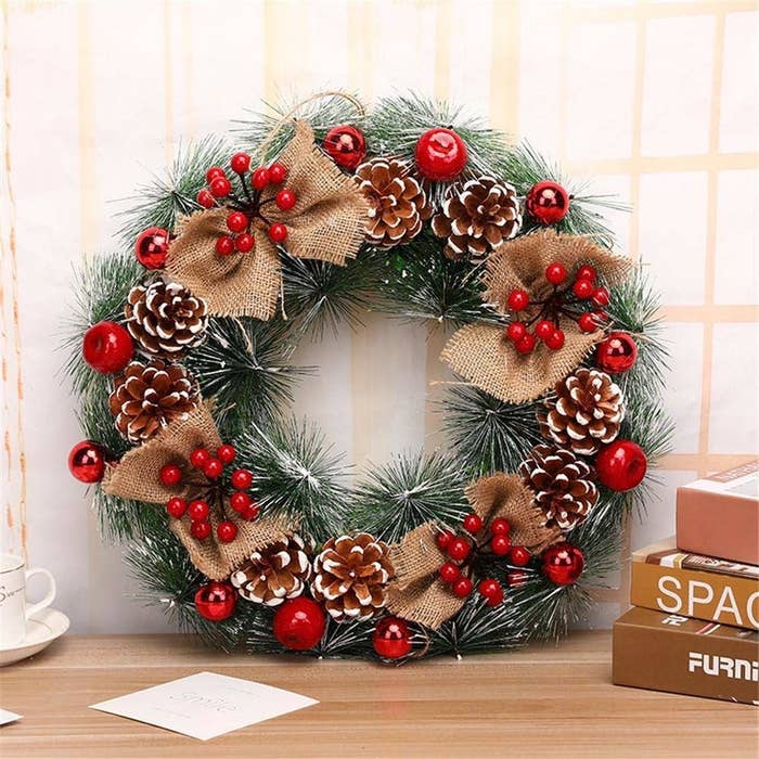 A wreath made out of fake white-tipped pine, holly berries, cherries, red baubles, pinecones, and burlap bows.