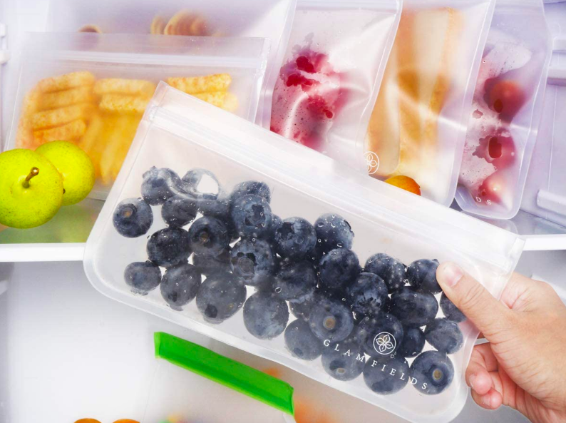 Person holding baggie with blueberries in front of fridge with several matching bags stored upright behind it 