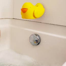 Yellow silicone duck covering bath faucet with open beak covering drain plug 