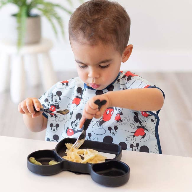 Child eating while wearing tee style smock with short sleeves and food-catching pocket in center 