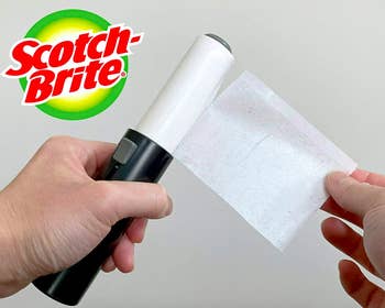 Handheld lint roller with fuzz-covered end being removed 