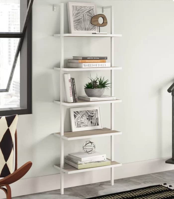 White 5 tiered bookcase with various books, frames and decorative items