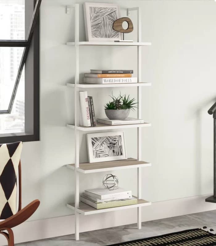 White 5 tiered bookcase with assorted  books, frames and decorative items
