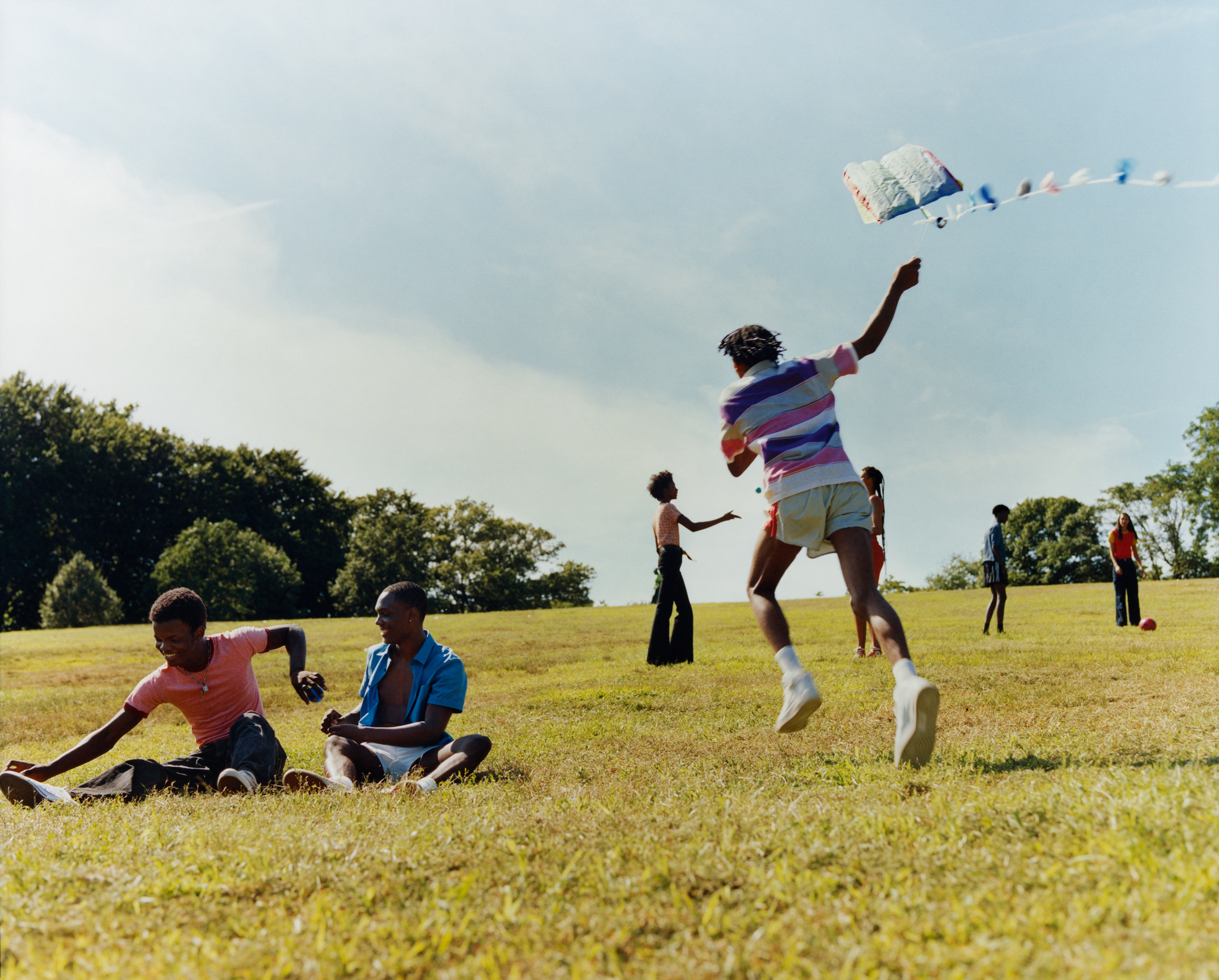 Young teenagers running and playing in a field under a blue sky. 