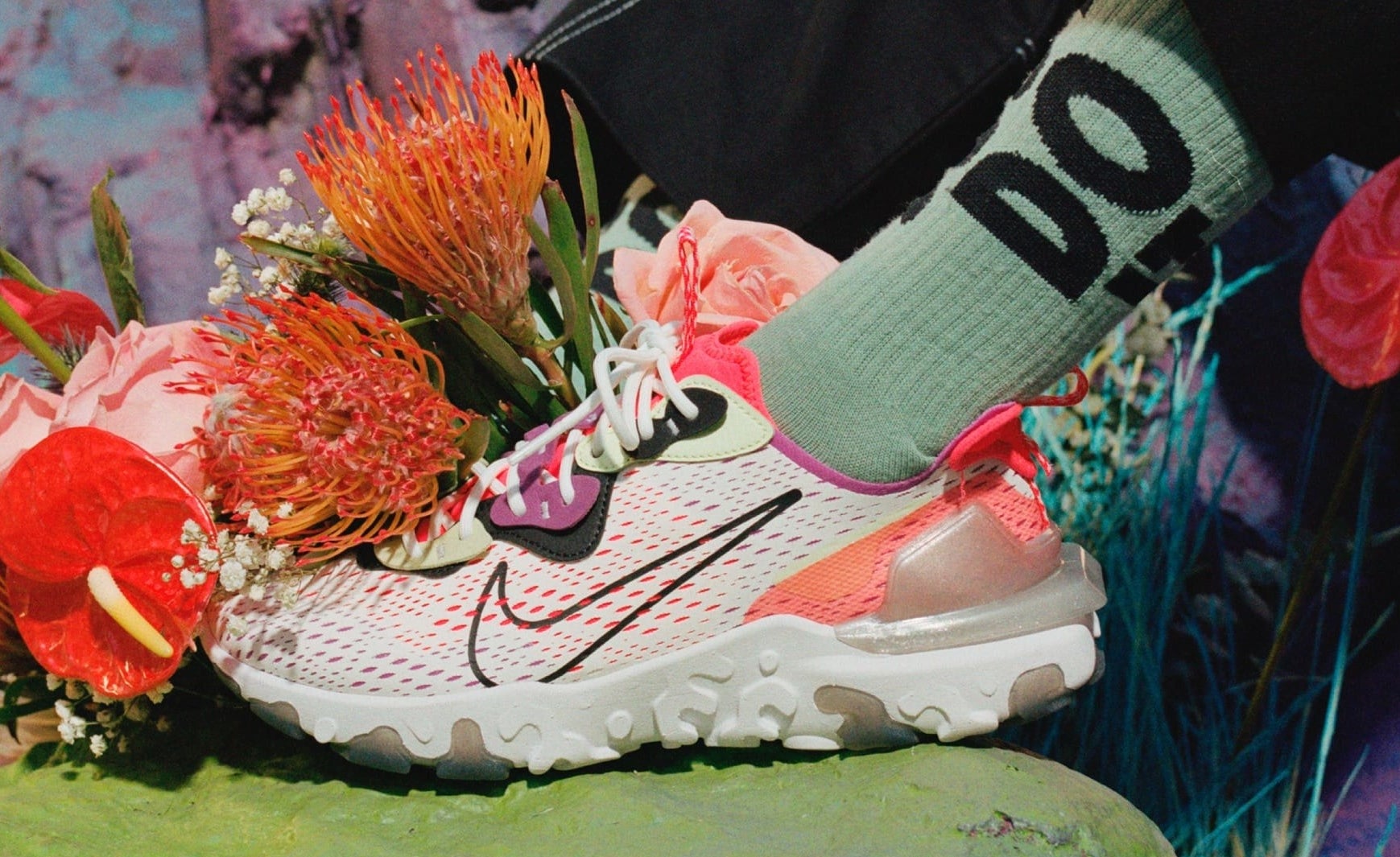 Model wears pink and white Nike React Vision shoe with &quot;Just Do It&quot; green socks