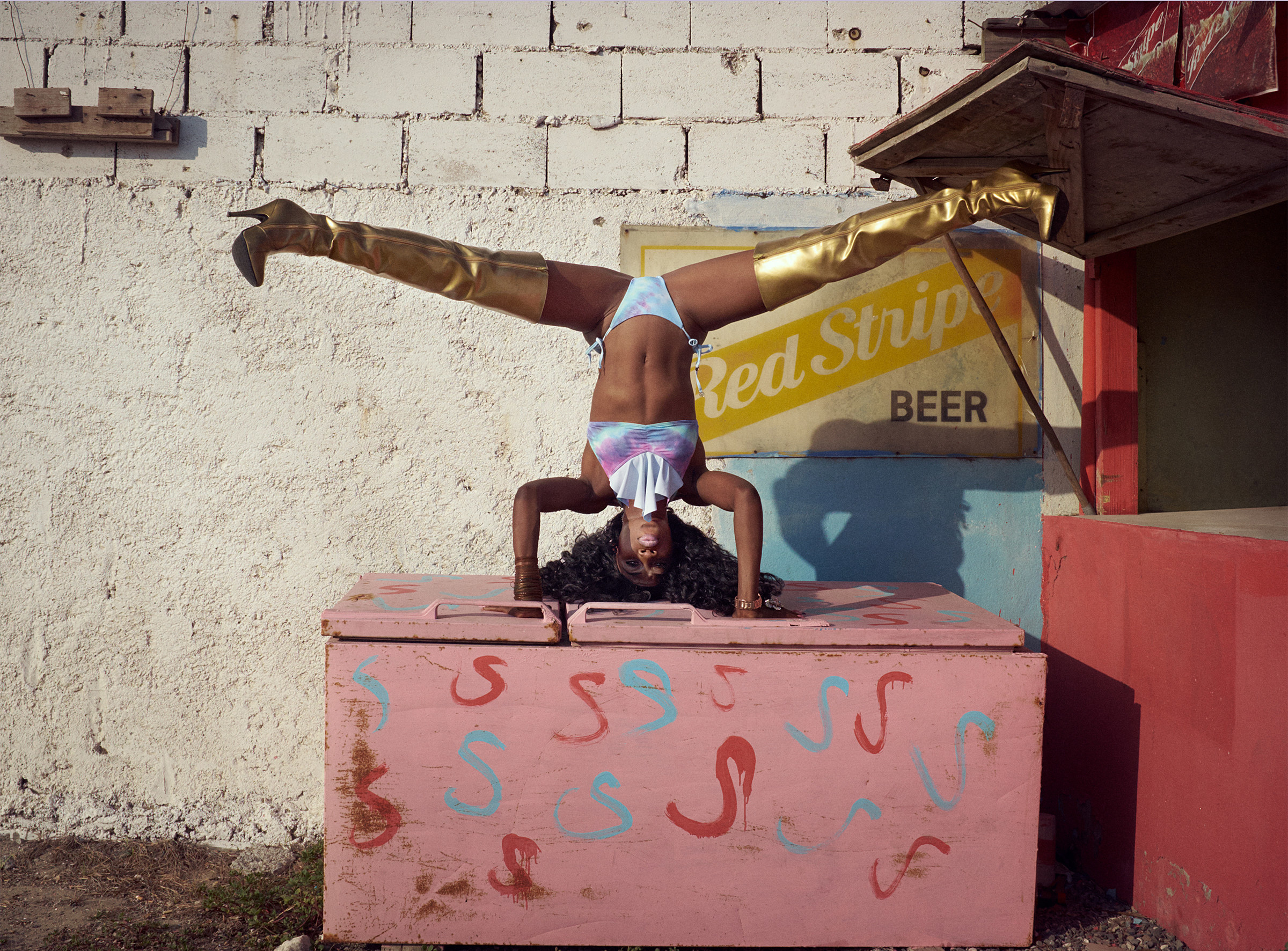 A woman in gold boots doing a handstand on a pink box