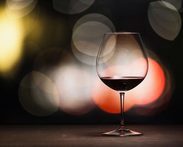 A glass of red wine placed on a table before a wall of twinkling winter lights