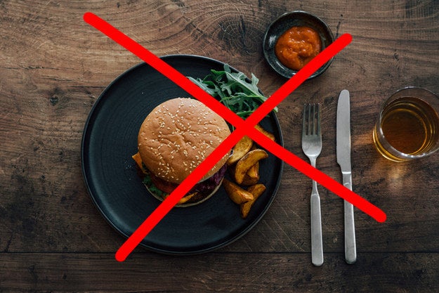 A burger sitting on a plate next to some fresh fries but they're crossed out with an X