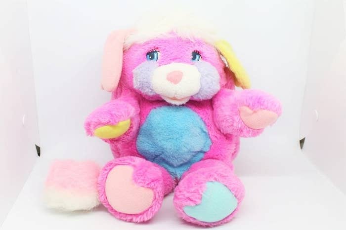 A pink, purple, and blue Popple sitting in a white box