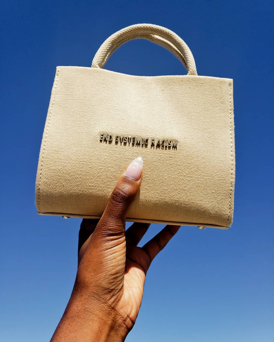 BuzzFeed writer holding the mini tote bag that says "End systemic racism"