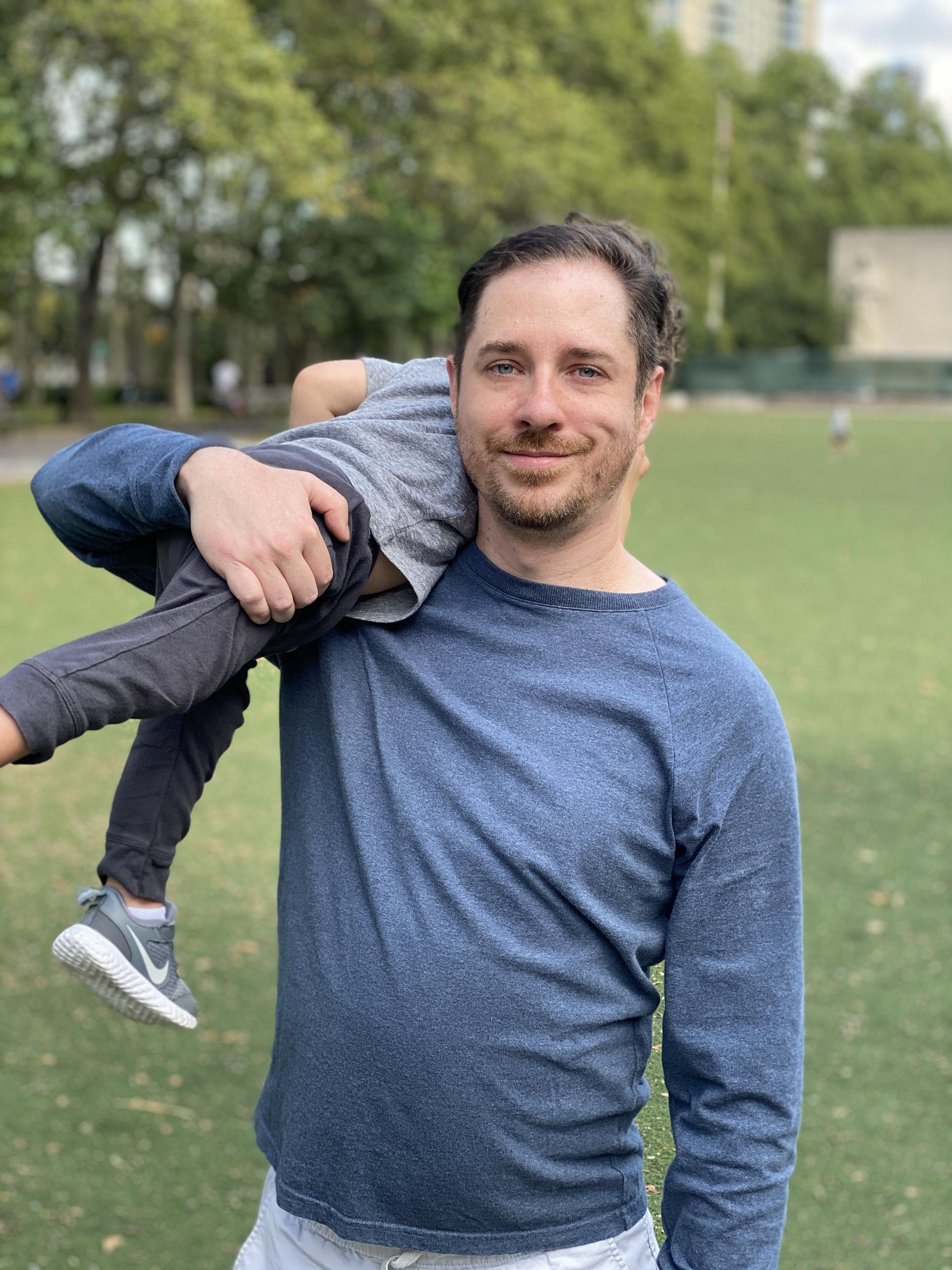 john holding his kid over his shoulder in a park