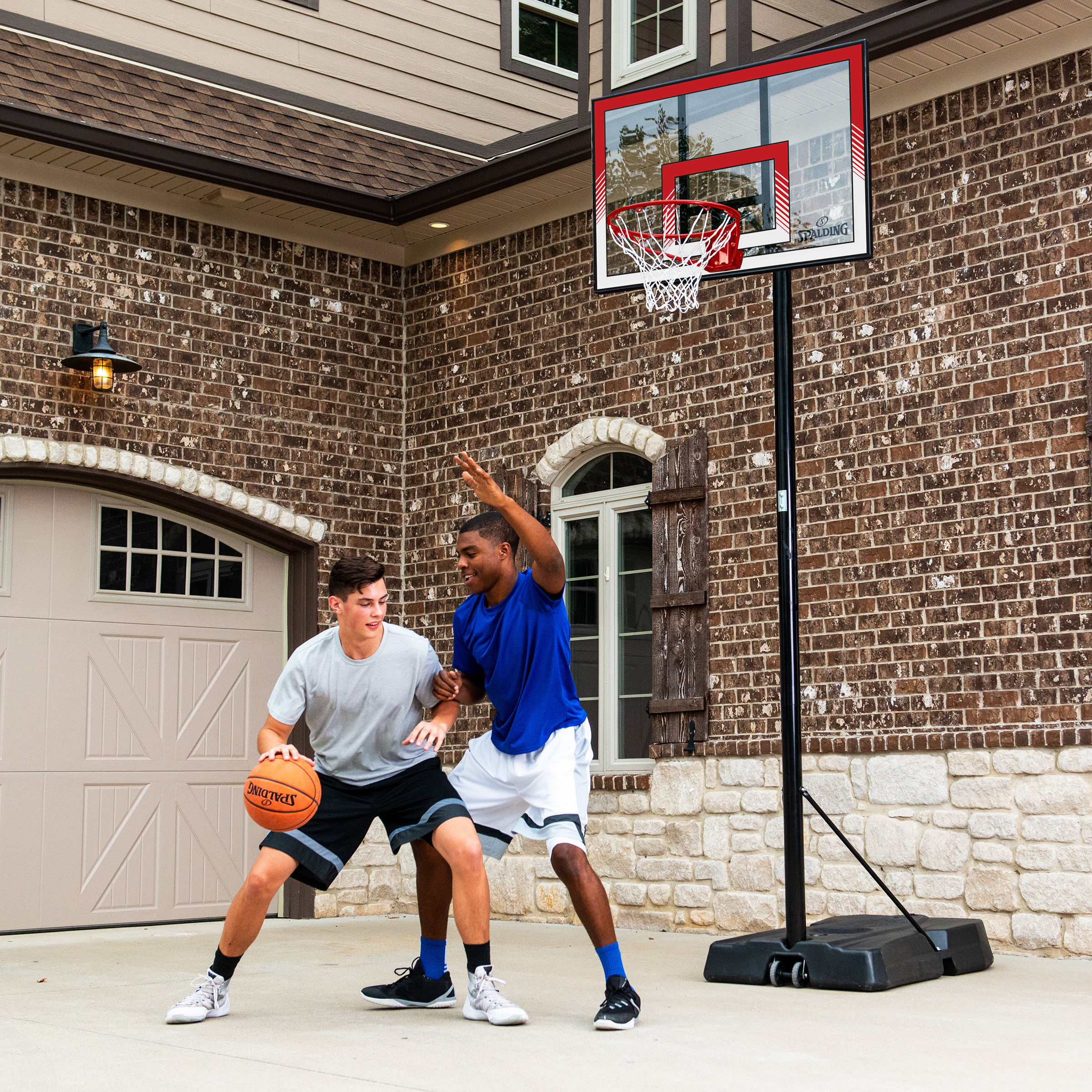 two teenagers playing basketball in front of an adjustable basketball hoop