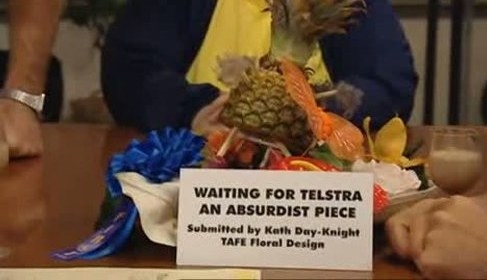 A piece of art with a sign that reads &quot;Waiting for Telstra: An Absurdist Piece, submitted by Kath Day-Knight, TAFE Floral Design&quot;