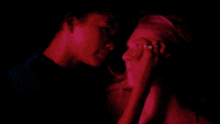 Rue and Jules hold each other&#x27;s faces in the dark as colorful lights flash periodically. 