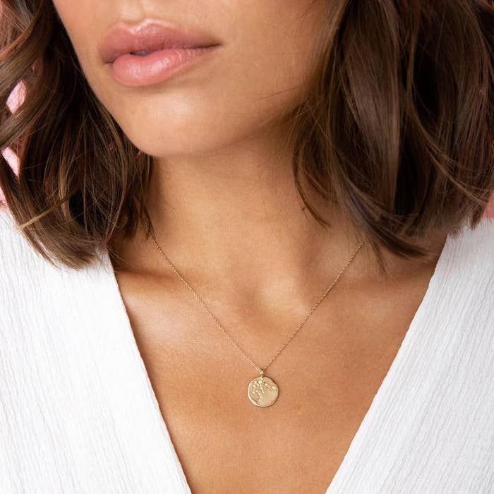 a model wearing a gold necklace with a gold pendant that has an astrological constellation etched into it