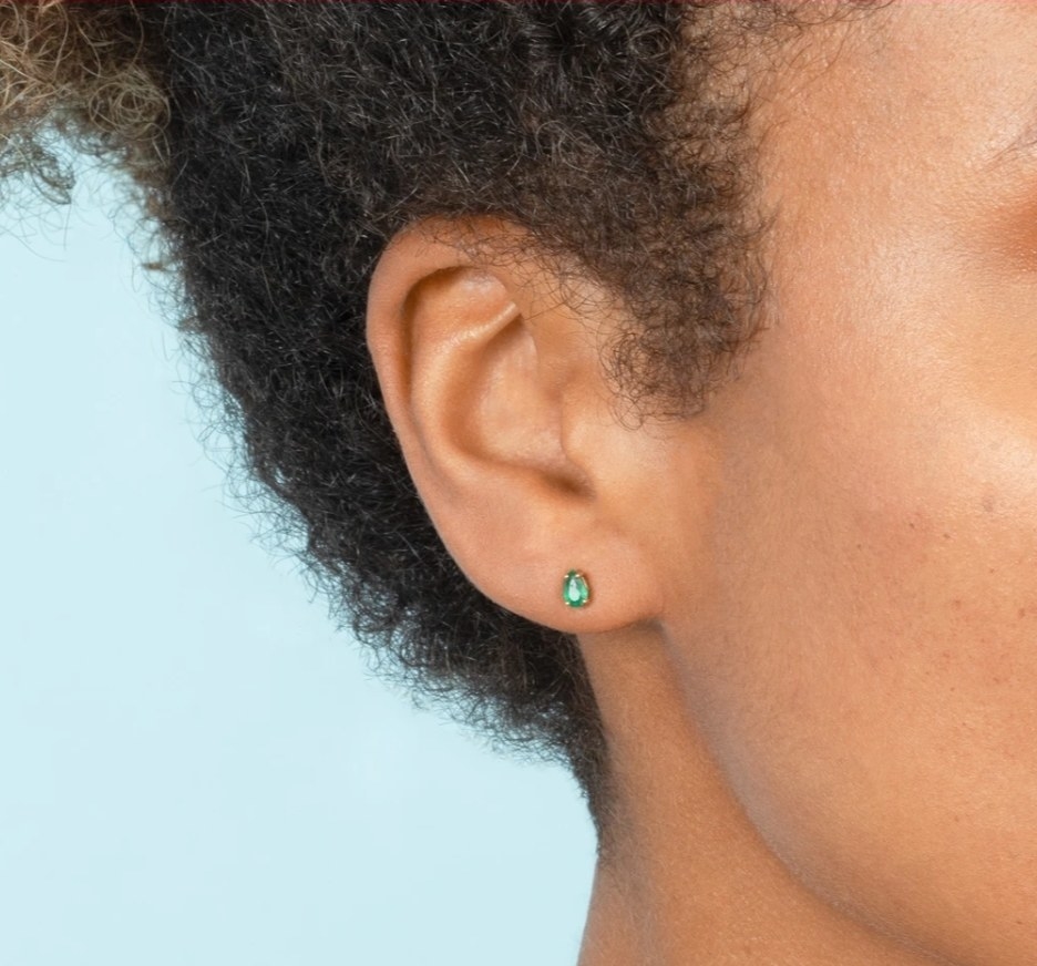 a model wearing an emerald pear shaped stud in their ear lobe