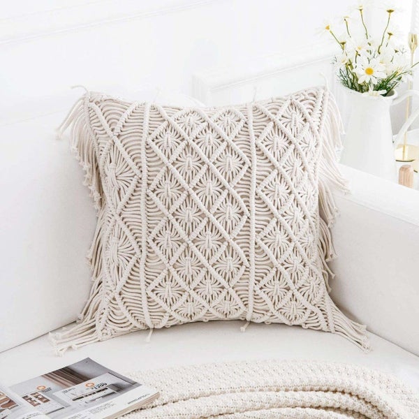 A beige macrame cushion kept on a beige couch.