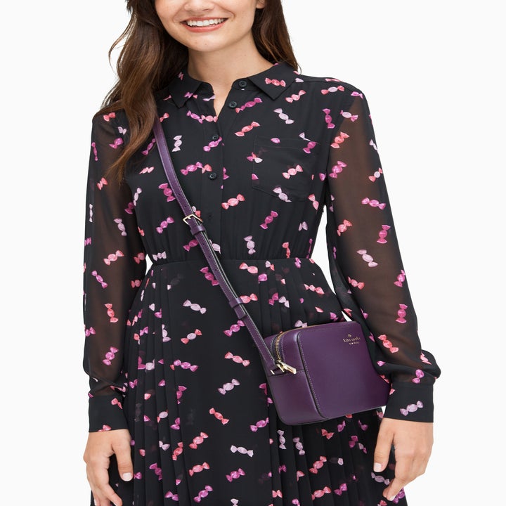 Model wears dark purple crossbody bag across sheer black dress with candy print