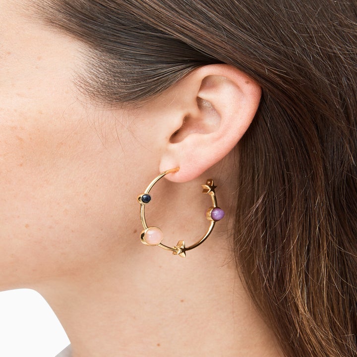 Model wears gold hoop earrings with small black, pink, and purple circles