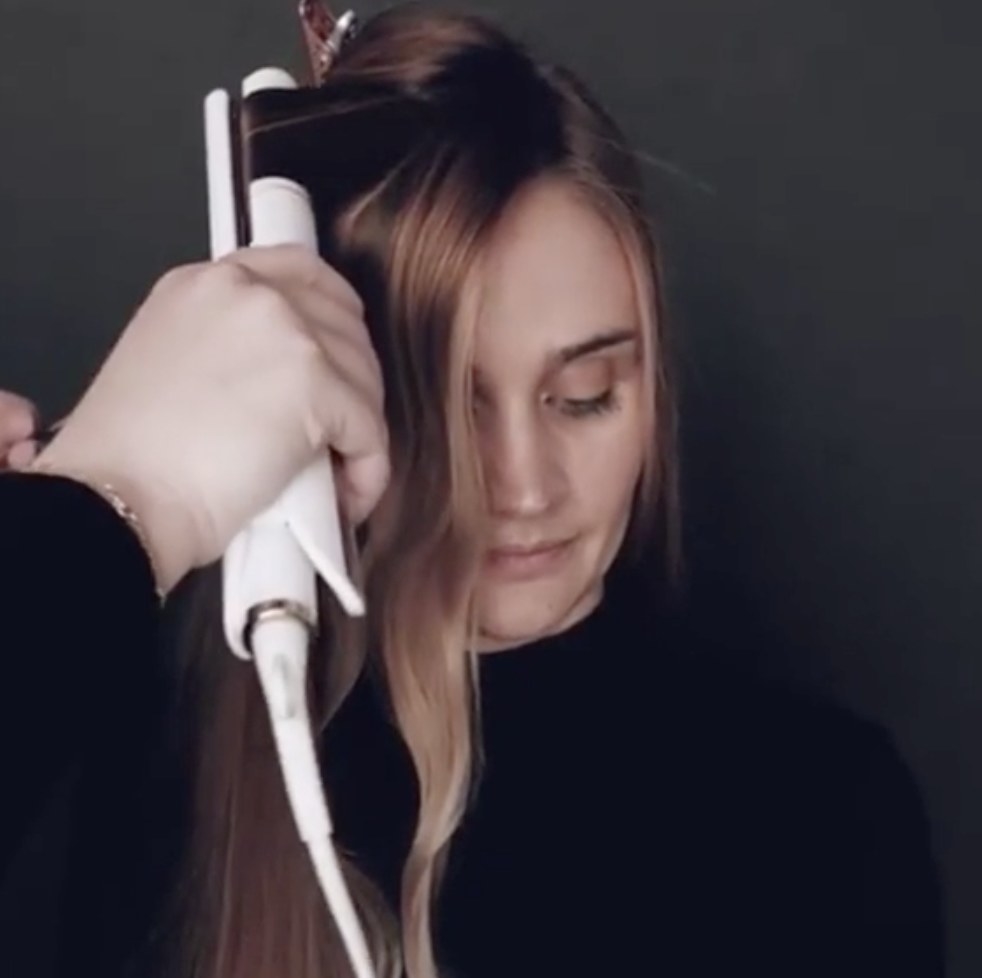 A person curling hair with a flat iron